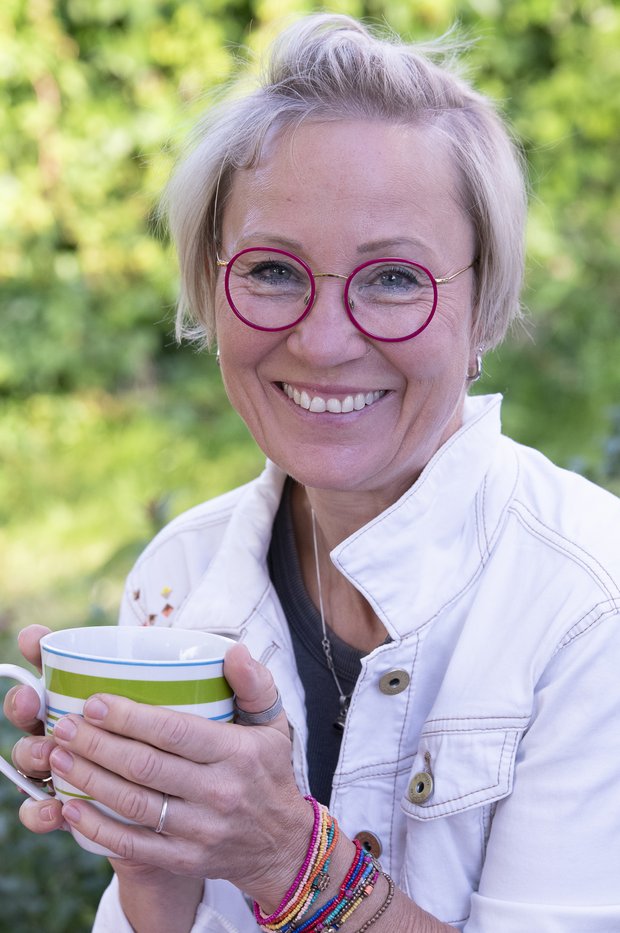 Portrait von Simone Tonn. Sie lächelt in die Kamera und hält eine Tasse in der Hand.
